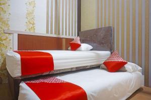 two beds in a hotel room with red and white pillows at Hotel O Sari Jeneponto in Jeneponto
