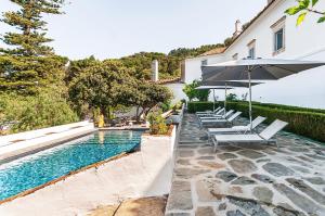 a pool with chairs and an umbrella next to a house at Convento Sao Paulo - Hotel Rural in Aldeia da Serra