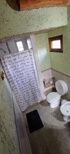 a bathroom with two toilets and a sheet of writing on the wall at Cabaña Esquina Siracusa in Villa Yacanto