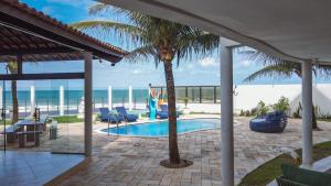 a swimming pool with a palm tree and the ocean at Brisa Atlantica in Barra de São Miguel