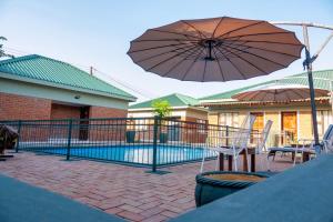un patio con sombrilla, sillas y piscina en Victoria Falls Premier Lodge, en Victoria Falls
