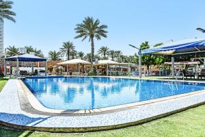 a large swimming pool with palm trees and umbrellas at OYO 138 Gulf Sand Motel in Barka