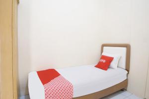 a small bedroom with a white bed with two red pillows at Hotel O Kost Ketapang Syariah in Medan +18 photos