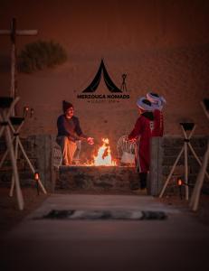 a couple of people standing around a fire at Merzouga Nomads Camp in Merzouga