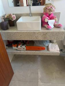 a doll sitting on a shelf under a sink at Casa em condomínio rural in Rancho Queimado