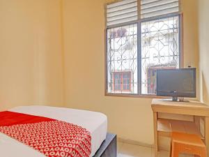 a bedroom with a bed and a desk and a window at Hotel O Excellent Kost in Jambi