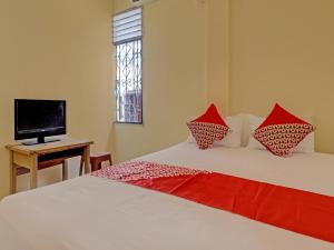 a bedroom with two beds with red pillows and a television at Hotel O Excellent Kost in Jambi