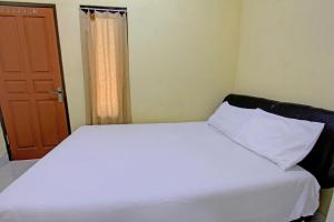 a bedroom with a white bed and a brown door at Hotel O Kos Moncok in Tjakranegara