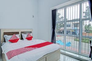 a bedroom with a bed with red pillows and a large window at Hotel O Lestari Baru Syariah Near SMA Negeri 1 Salo in Bangkinang