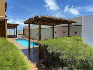 a swimming pool with a straw umbrella next to a house at Varanda do Oceano Maracajaú in Maxaranguape