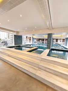 - une grande piscine avec parquet dans un bâtiment dans l'établissement Apto com lazer completo, piscina, ar, mercadinho e pet friendly a 1 min da praia, à Praia Grande