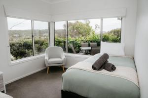 ein Schlafzimmer mit einem Bett und einem Stuhl und Fenstern in der Unterkunft Port Campbell Coastal Unit 2 in Port Campbell