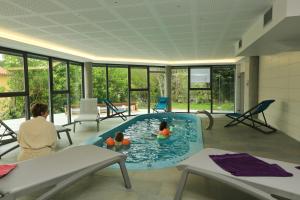 two children in a swimming pool in a room with windows at Logis Hotel Spa Restaurant Le Provence in Lanarce