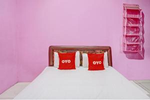 a bed with two red pillows in a purple room at OYO 93114 Salak Homestay Syariah in Plosobegem