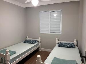 two twin beds in a room with a window at Apartamento Maitinga aconchegante in Bertioga