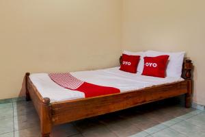 a wooden bed with two red pillows on it at Hotel O Pondok Wisata Sekar KemuningNearWonogondang Camp ( Bumi Perkemahan Wonogondang ) in Yogyakarta