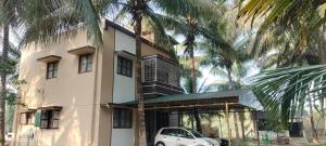 a white car parked in front of a building with palm trees at KV Farm house in Malaiyāndipattanam