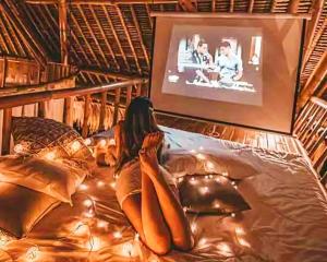 a woman laying on a bed watching a tv at La Royale Nusa Penida in Nusa Penida
