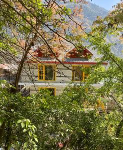 a house with yellow windows and a mountain in the background at Dahar Retreat - A Boutique Homestay in Kotla
