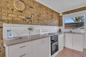 a kitchen with white cabinets and a brick wall at Lakeside Apartments 7 in Merimbula