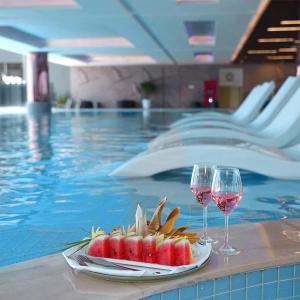 two glasses of wine and a plate of fruit next to a swimming pool at Lynn Times Thanh Thuỷ Hotel in Xuân Vi