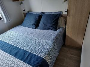 Una cama con almohadas azules en una habitación pequeña. en Charmant mobil-home 178, en Narbona