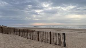a wooden fence on a beach with the ocean at Petit cocon avec terrasse à 150m de l'océan in Soulac-sur-Mer +5 photos