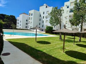 a lawn with umbrellas in front of a building at Anc14 Apartamento con 2 habitaciones, patio y piscina al lado de la playa in El Puerto de Santa María