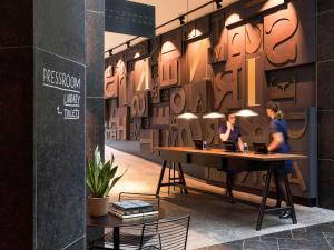 アムステルダムにあるINK Hotel Amsterdam - MGallery Collectionの文字の壁のある部屋で働く女性2人