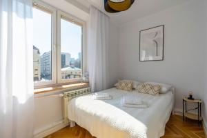 a white bedroom with a bed and a large window at Wola Ratusz Serene Apartment by BookingHost in Warsaw