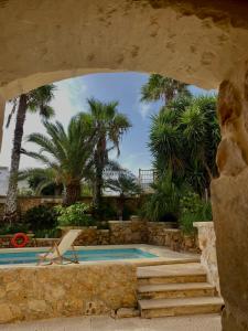 a swimming pool with a chair and palm trees at Ta' Tereża Farmhouse in Xagħra