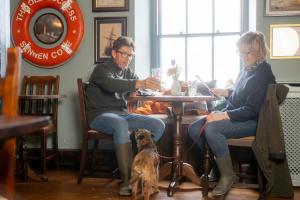 a man and woman sitting at a table with a dog at The Old Success Inn in Sennen Cove