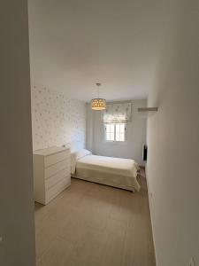 a white bedroom with a bed and a window at Apto moderno y familiar junto al mar in Torrox