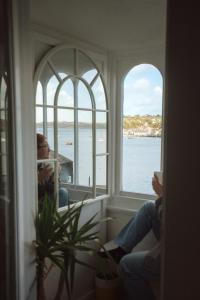 a woman sitting in a window looking out at the water at Breathtaking High Street Townhouse With Stunning Sea Views at 'The Old Fishermans Townhouse' in Falmouth