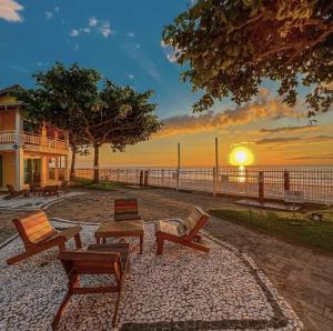 a group of chairs and a table with the sunset at Pousada Vila ÁguaMar in Itapoa