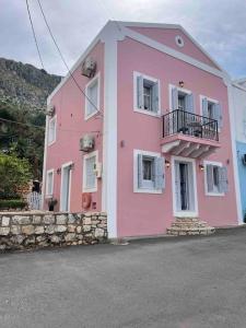 a pink house with white windows on a street at Kastelorizo suites in Meyisti