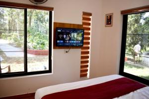 a bedroom with a tv on the wall and two windows at Green Heaven Kuruva Wayanad in Chekadi