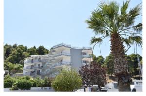a tall white building with a palm tree in front of it at Alexandros Kalamos Hotel in Áyioi Apóstoloi