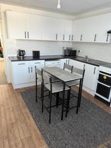 a kitchen with white cabinets and a table and chairs at Beautiful-2 bedroom Apartment, 1 bathroom, sleeps 6, in greater london (South Croydon). Provides accommodation with WiFi, 3 minutes Walk from Purley Oak Station and 10mins drive to East Croydon Station in Purley