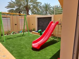 een rode glijbaan in een speeltuin met groen gras bij Pool House at Janabiyah in Al Janabīyah
