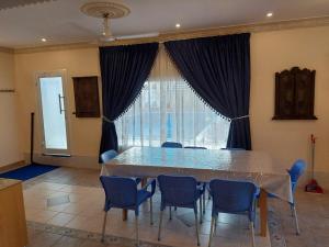 een eettafel met blauwe stoelen en een groot raam bij Pool House at Janabiyah in Al Janabīyah