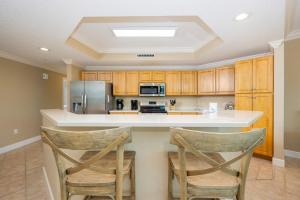 a kitchen with wooden cabinets and a counter with two chairs at Phoenix on the Bay 1429 condo in Orange Beach