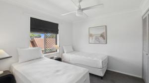 Una habitación blanca con dos camas y una ventana. en Barefoot On First - Pool, Beach, Family - Friendly, en Sawtell