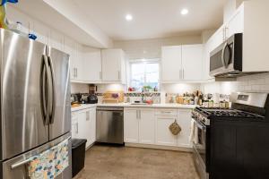 a kitchen with white cabinets and a stainless steel refrigerator at Beautiful Vancouver Cedar Cottage House in Vancouver