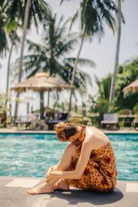 a woman in a dress sitting next to a swimming pool at Isolabella Ayurveda Hotel Hiriketiya in Nilwella
