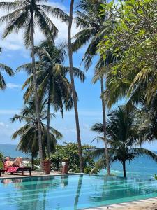 a person laying in a chair next to a swimming pool with palm trees at Isolabella Ayurveda Hotel Hiriketiya in Nilwella +3 photos