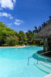 a swimming pool at a resort with a thatch roof at Villa Corail - Premier repas offert sur place in Cap Malheureux