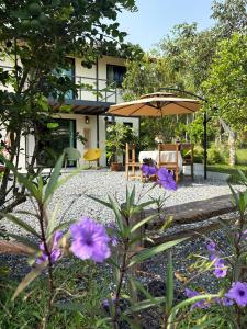 un patio con sombrilla y algunas flores púrpuras en Uma Valley Homestay - Nature Oasis near Hay Yai, en Ban Wang Ching