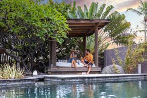 un homme et une femme assis sur un banc à côté d'une piscine dans l'établissement Villa Taika, à La Saline les Bains