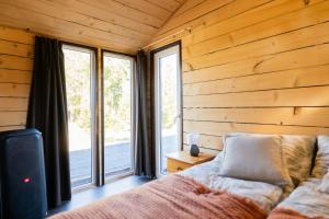 a bedroom with wooden walls and a bed and windows at Meža namiņš Upeskrasti in Zosuļi